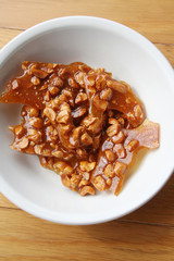 Peanut brittle pieces on a white bowl on wooden table