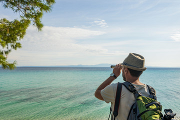 Obraz premium Closeup view photography of male tourist looking through old vintage telescope far away in distance at beautiful seascape of Aegean sea in Greece landscape.