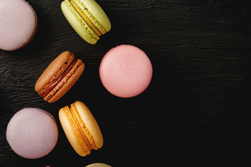 Macaroni cookies of different colors lie on a black textured background. Free space. Still life of confectionery.