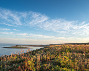 Autumn landscape of the sea coast , blue sky with beautiful clouds, the coast overgrown with autumn colorful shrubs.