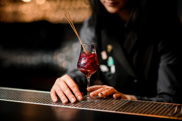 Close-up wineglass with red cocktail which decorated by two sticks stand on bar counter.