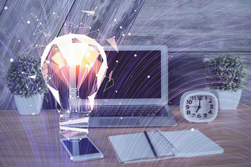 Computer on desktop in office with bulb icon hologram. Multi exposure. Concept of idea.