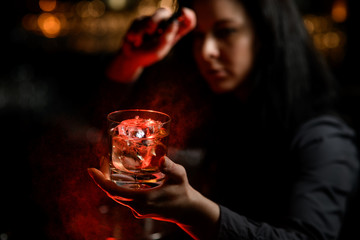 woman bartender holds by hand glass with drink and spray on it.