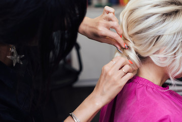 hands of a hair stylist with an invisible hairpin do the hair of a blonde girl