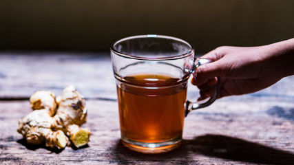 Girl's hand hold a glass of ginger tea on wood table. Concept of herbal medicine from Asia which contains antioxidants is believed to be good for health. Zingiber officinale.