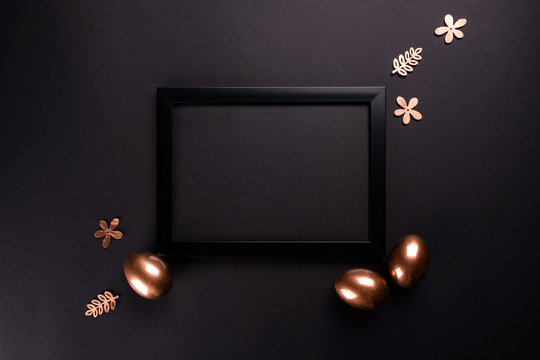 Easter background with black fhoto frame and gold Easter eggs on black background. Flat lay, Top view, mockup, copy space.