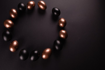 Golden and black eggs, laid out in a circle on black background. Flat lay, Top view, copy space.