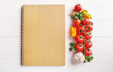 Recipe book and vegetables on white wooden background