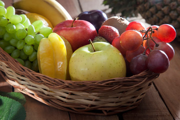 Wicker basket filled with fresh fruits against wooden background