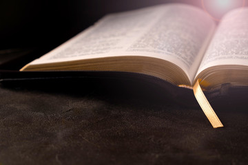 Open Bible on a dark table with light coming from above. Christianity concept. Holy Bible background.