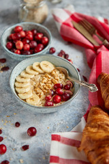 Ceramic bowl of oatmeal porridge with banana, fresh cranberries and walnuts