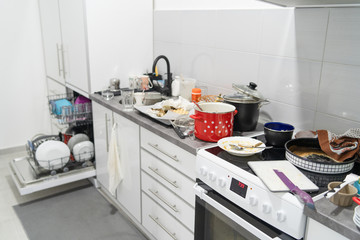 Side view on white kitchen with unwashed dirty pots and dishes on the countertop utensils and...