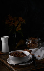 Chocolate granola in white bowl. Dark key photo style. cozy home, homemade breakfast