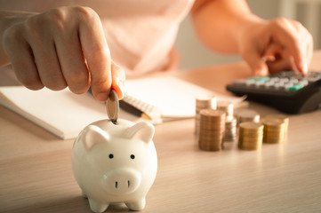 Woman hand putting money coin into piggy for saving money. Record income and expenses to save...