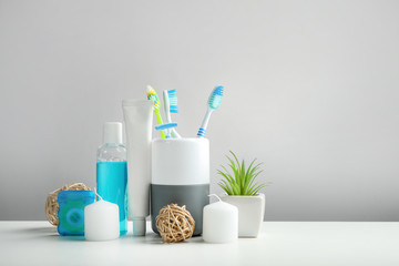 Toothbrushes in cup and other dental products on grey background