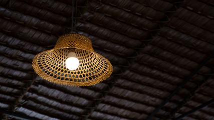Low angle view of vintage hanging lamp decoration with bamboo farmer's hat against straw roofing...