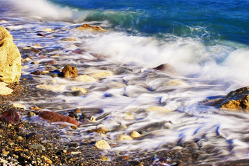 Sea pebbles in coastal sea waves. The shore plays with paints in the sunlight.