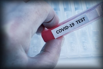 Obraz premium A hand in a protective glove holds a test tube labeled COVID-19 with red liquid against a background of a number of clean medical tubes. The problem of the spread of coronavirus infection