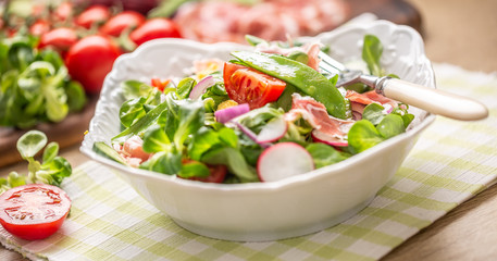 Fresh spring salad with green leaves tomatoes egg radish red onion young peas prosciutto feta cheese and olive oil