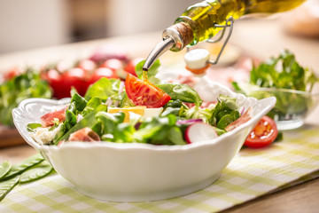 Bottle with olive oil pouring into salad