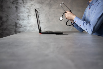 Lekarz ze stetoskopem w dłoni przed komputerem na betonowym tle - obrazy, fototapety, plakaty