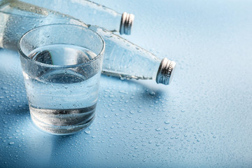 Glass water bottles and glass of water on blue background