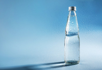 Glass water bottle on blue background