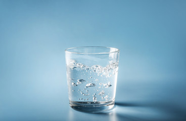 Water pouring from plastic bottle in glass on blue background