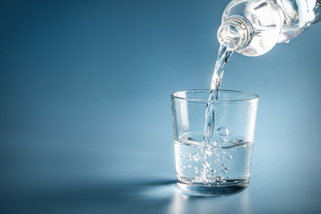 Water pouring from plastic bottle in glass on blue background