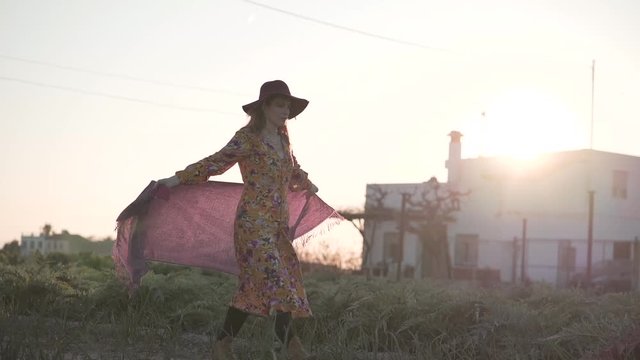Stylish woman in hat walking on field in summer
