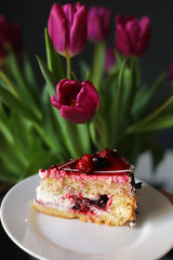Close up of slice of berry cake on a white plate near beautiful tulips flowers. holiday. birthday cake.