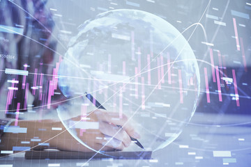 A woman hands writing information about stock market in notepad. Forex chart holograms in front. Concept of research. Double exposure