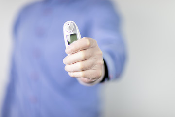 Lekarz w niebieskiej koszuli na jasnym tle trzymający w dłoni termometr