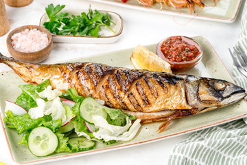 Grilled fish served with sauce, lemon, and fresh vegetables