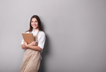 Fototapeta premium Young woman holding notebook i on gray background.