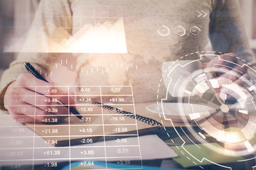 Forex chart hologram on hand taking notes background. Concept of analysis. Double exposure