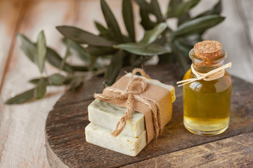 Concept of natural ingredients in cosmetology for gentle skin care. Organic olive oil in glass bottle, handmade soap bars. Atmosphere of serenity and relax. Rustic wooden background, close up.