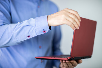 Mężczyzna w niebieskiej koszuli trzymający czerwony laptop w dłoniach na jasnym tle - obrazy, fototapety, plakaty