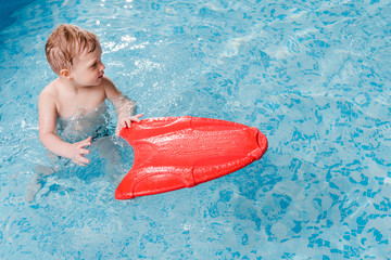 cute toddler boy swimming with flutter board in swimming pool