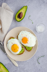 Avocado toast with fried egg and sea salt on a plate on a grey background. A healthy breakfast or lunch. Vertical orientation.