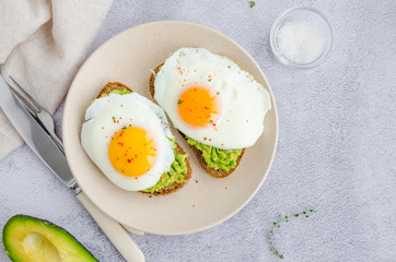 Avocado toast with fried egg and sea salt on a plate on a grey background. A healthy breakfast or lunch. Horizontal orientation.