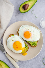 Avocado toast with fried egg and sea salt on a plate on a grey background. A healthy breakfast or lunch. Vertical orientation.