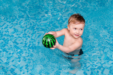 cute toddler boy swimming with inflatable ball in swimming pool