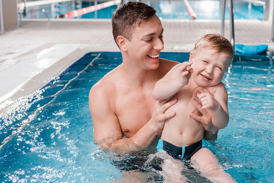 happy trainer holding in arms toddler kid in swimming pool