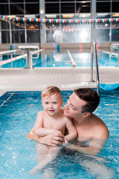 happy swim coach looking at cute toddler boy in swimming pool