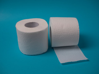 Two rolls of white perforated two-layer toilet paper isolated on a blue background close-up.