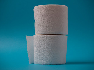 Two rolls of toilet paper stand on top of each other on a blue background close up.