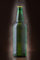 Bottle of beer covered by water drops on brown background