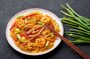 Singapore Mei Fun in white plate on dark slate background. Singapore Noodles is chinese cuisine dish with rice noodles, prawns, char siu pork, carrot, red onion, napa cabbage. Chinese food.