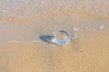 Fototapeta na wymiar 夏の海水浴場の砂浜にある透明な水晶ガラスボール